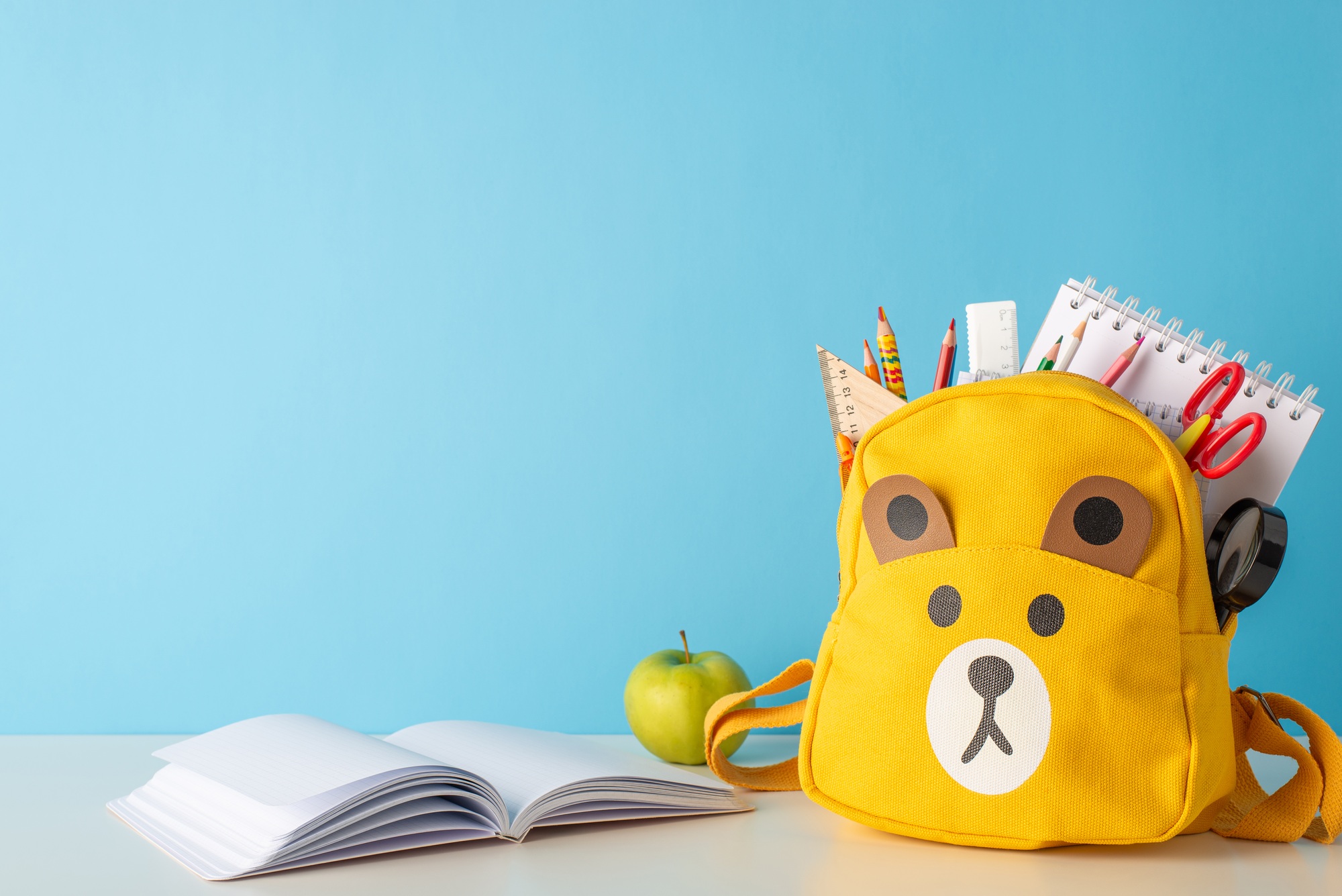 School organization. Side view photo of teddy-bear schoolbag filled with school essentials - pens